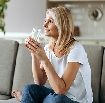 woman sitting on couch drinking glass of water
