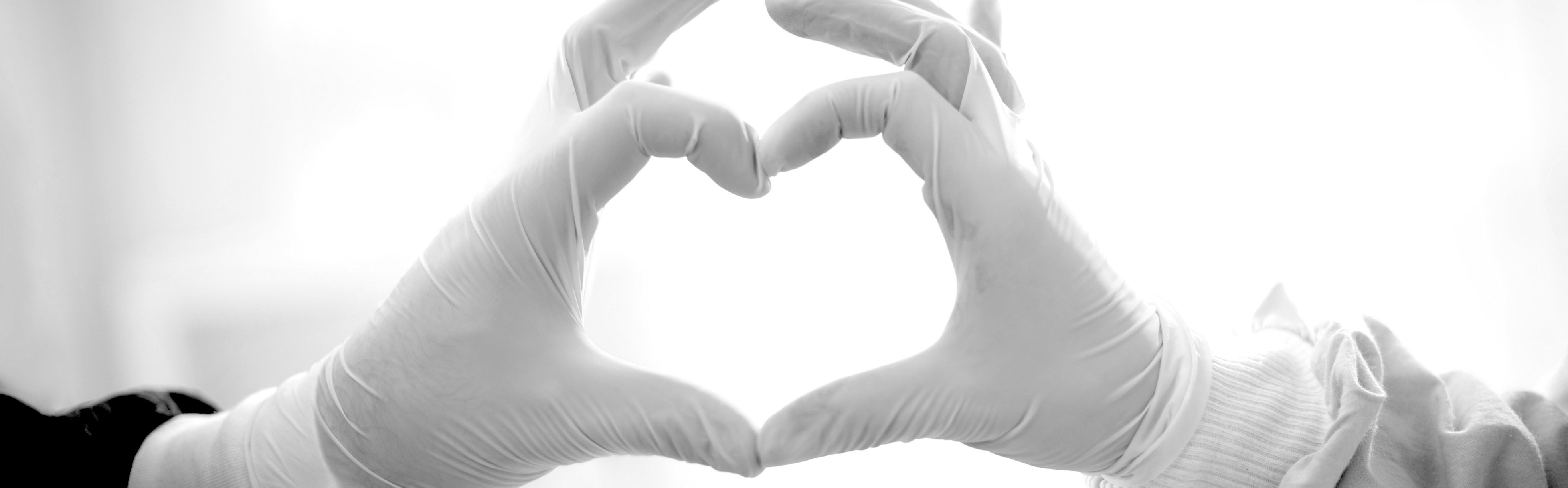 Healthcare workers hold up gloved hands to make a heart.
